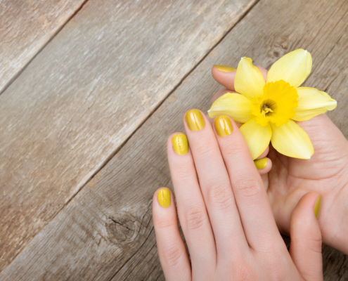 Yellow glitter manicure holding a flower